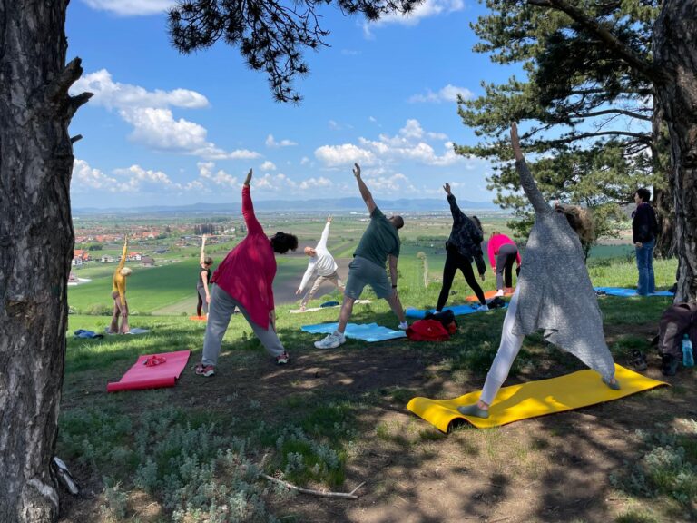 Grup practicând yoga în aer liber, pe un deal, cu câmpia în zare
