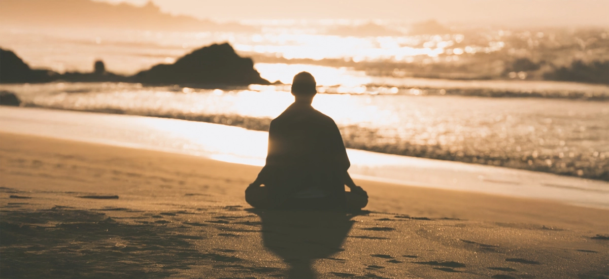 Siluetă în meditație pe malul mării, la apus