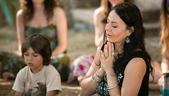 Femeie cu mâinile unite în semn de recunoștință, alături de un băiețel