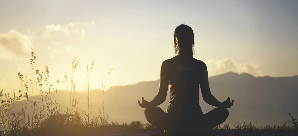 Siluetă așezată în meditație pe o culme, în lumina caldă a serii