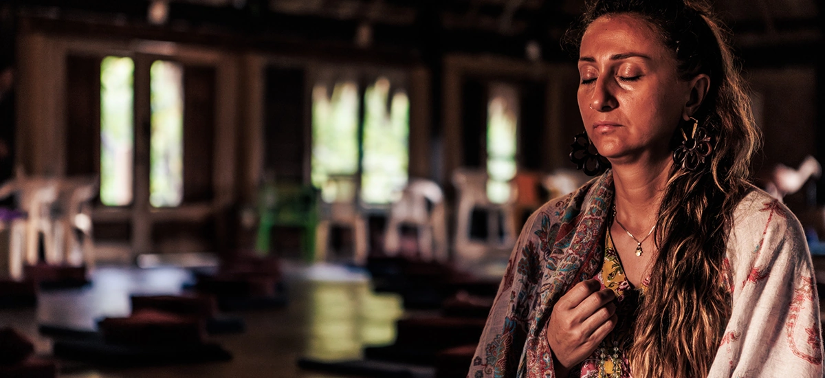 Femeie așezată în meditație, cu ochii închiși și mâna la Inimă